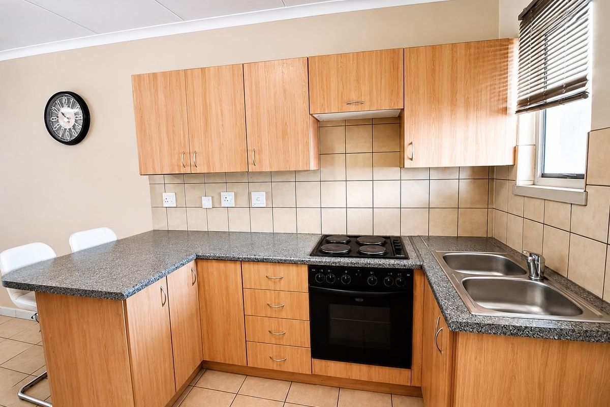 A functional kitchen featuring light wood-finish cabinetry, granite countertops, a built-in electric oven and hob, and a double stainless steel sink.