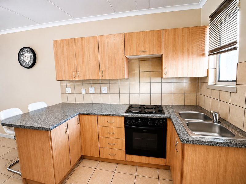 A functional kitchen featuring light wood-finish cabinetry, granite countertops, a built-in electric oven and hob, and a double stainless steel sink.