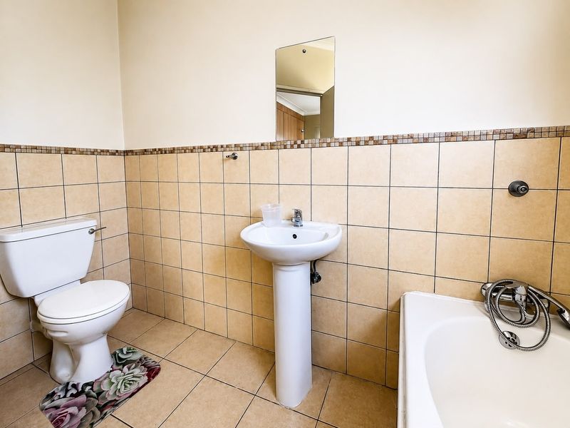 A functional bathroom featuring a pedestal basin, toilet, and bathtub with tiled walls and flooring throughout.