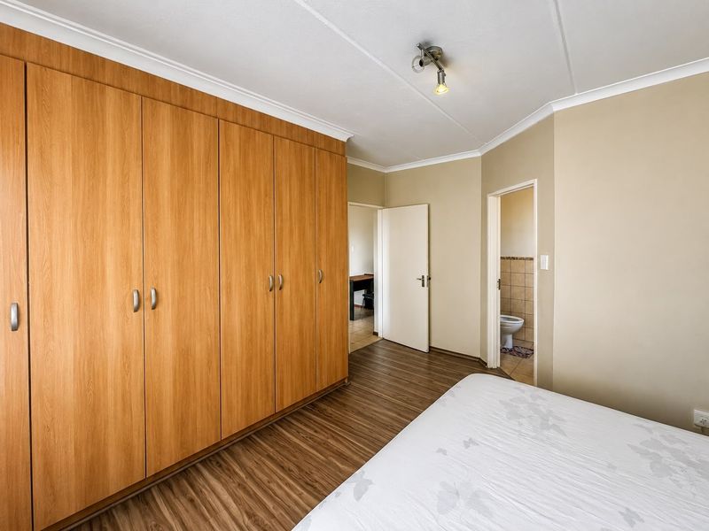 A bedroom featuring extensive built-in wooden cupboards, laminate flooring, and direct access to an en-suite bathroom.