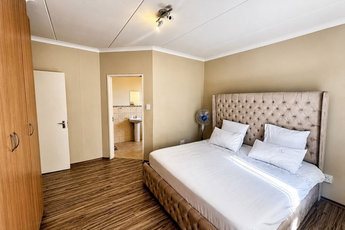 A well-maintained bedroom featuring laminate flooring, built-in wardrobe storage, and direct access to an en-suite bathroom.