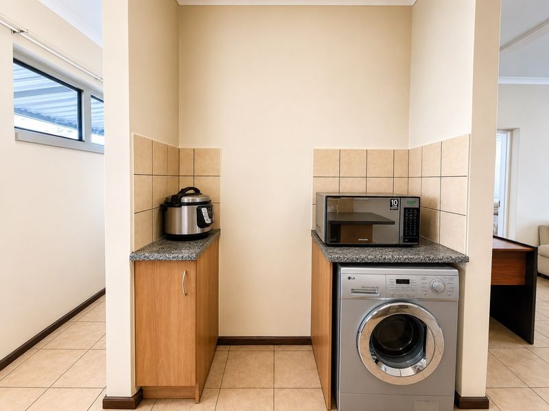 A functional laundry nook featuring built-in cabinetry, granite countertops, tiled splashbacks, and dedicated plumbing connections for a washing machine.