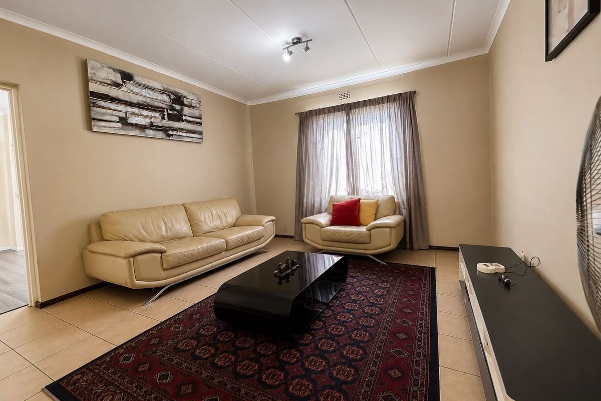 A well-lit living room featuring neutral wall tones, tiled flooring, and a large window with curtain rails.