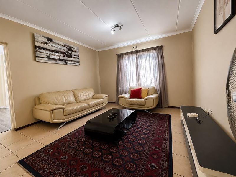 A well-lit living room featuring neutral wall tones, tiled flooring, and a large window with curtain rails.