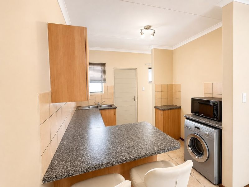 Functional kitchen featuring laminate cabinetry, granite-look countertops, tiled splashbacks, and integrated laundry facilities, offering a practical layout for daily use.