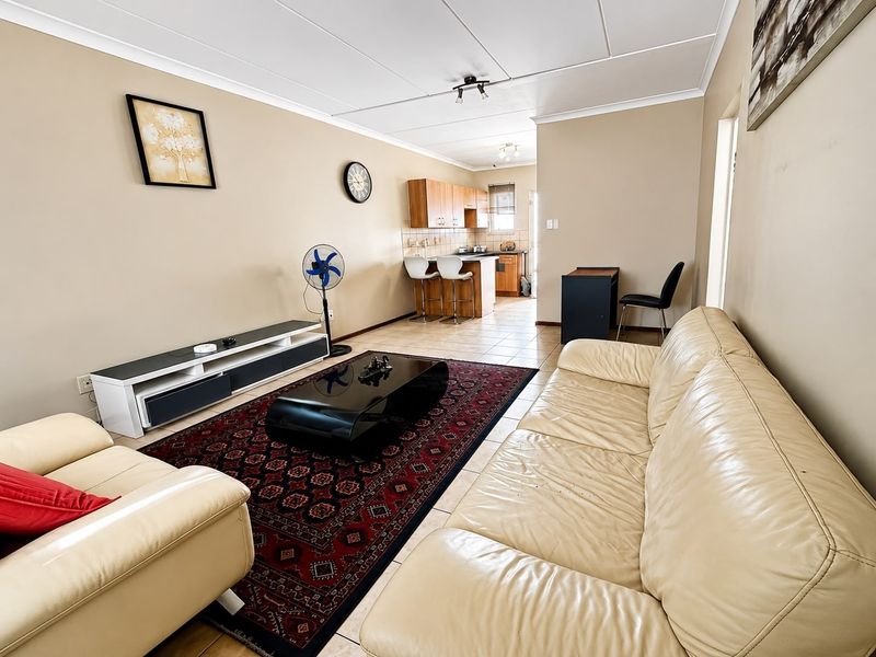 Open-plan living and kitchen area featuring tiled flooring, neutral wall tones, and a functional kitchen layout with breakfast bar seating.
