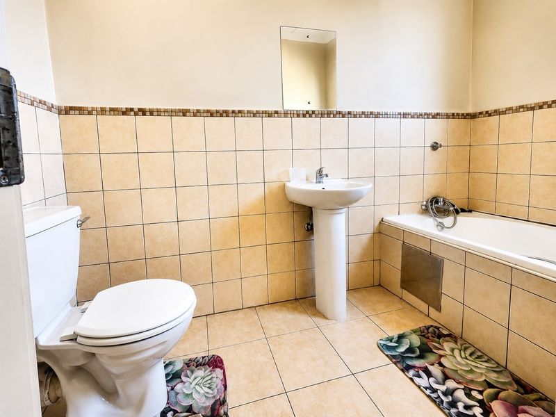 A functional bathroom featuring a pedestal basin, standard toilet, and a bathtub with tiled walls and flooring.