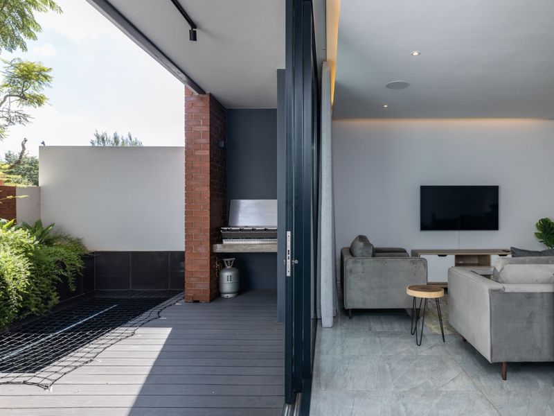 Modern covered patio featuring composite decking, a built-in braai, and seamless transition to the interior living area through large sliding glass doors.