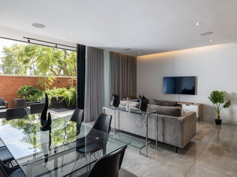 Modern open-plan living and dining area featuring large format floor tiles, recessed lighting, and seamless indoor-outdoor flow through expansive sliding glass doors.