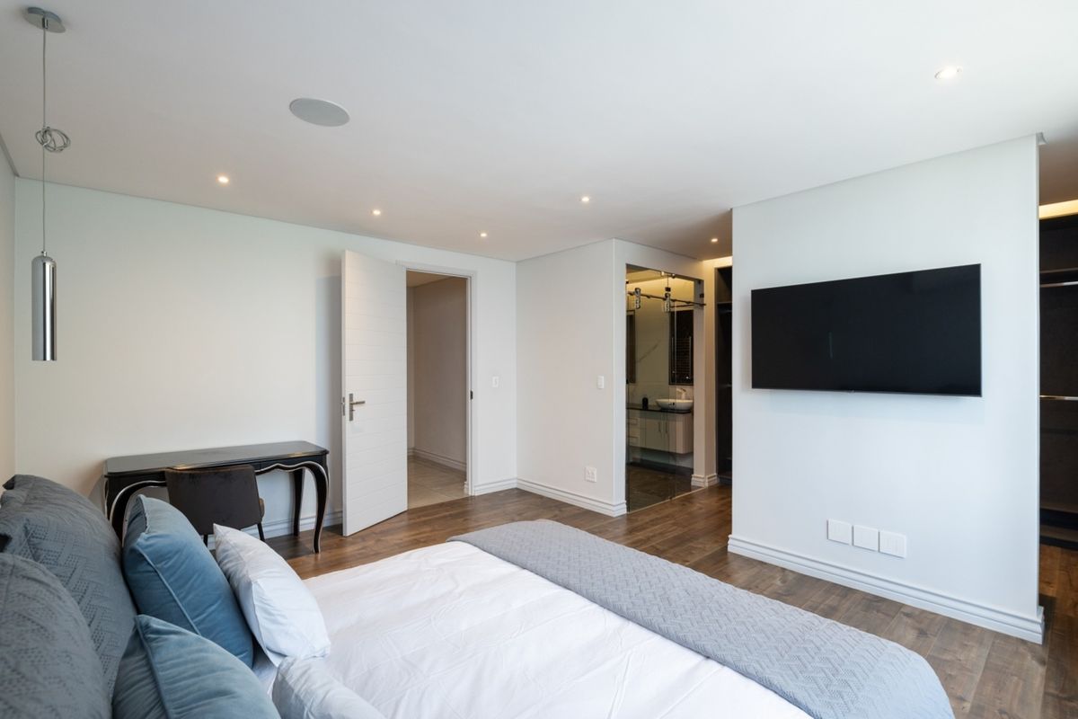 Modern bedroom featuring hardwood flooring, recessed ceiling lighting, integrated speakers, and direct access to an en-suite bathroom with a built-in wardrobe.