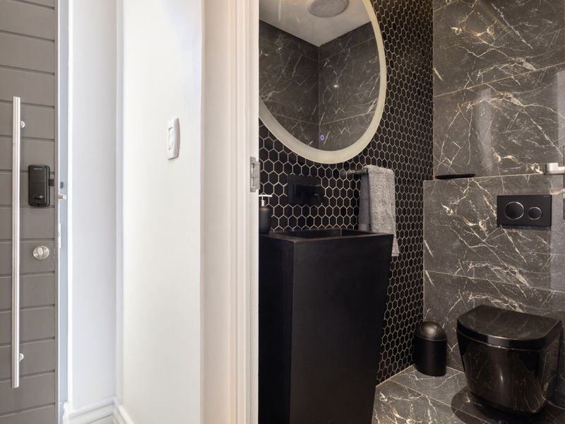 Modern guest bathroom featuring a sleek black pedestal basin, wall-mounted toilet with concealed cistern, and stylish dark marble-effect and hexagonal wall tiling.