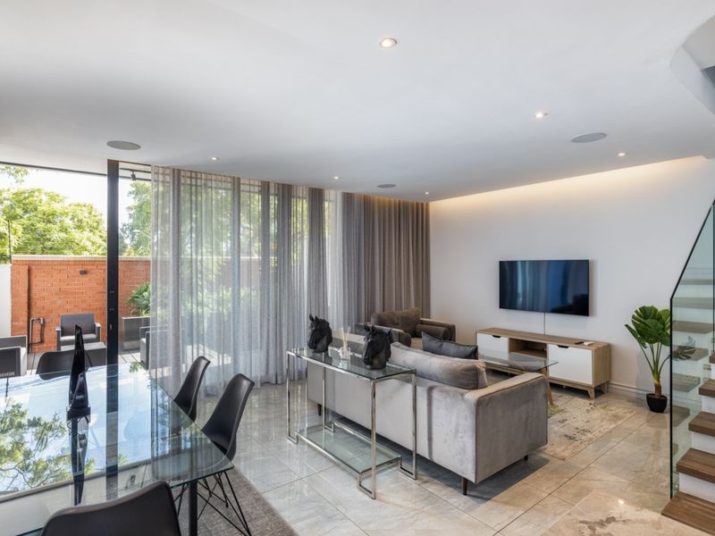 Modern open-plan living and dining area featuring tiled floors, recessed lighting, and a glass balustrade staircase with seamless access to the outdoor patio.