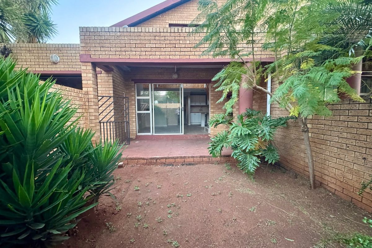 Rear view of the townhouse featuring a face brick facade, a covered patio area, and a small private garden space.