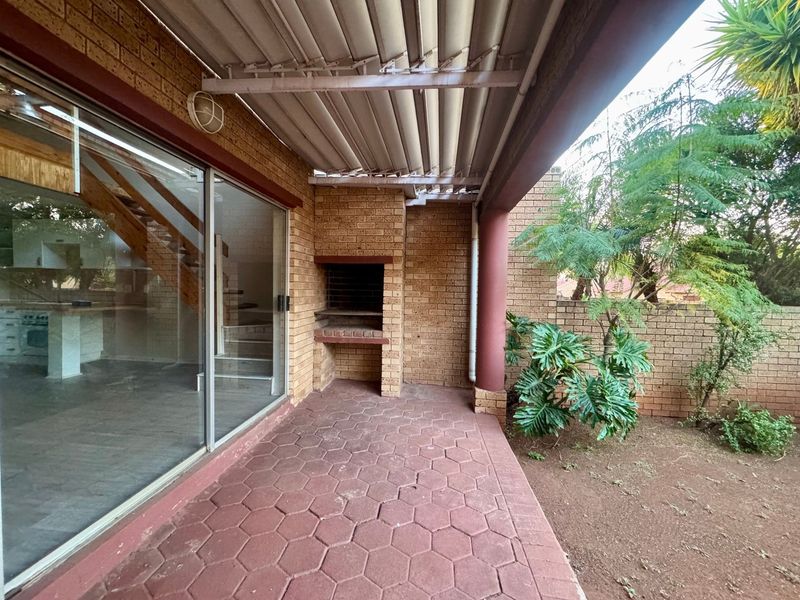 Covered outdoor patio featuring a built-in brick braai, paved flooring, and direct access to the interior through large sliding glass doors.