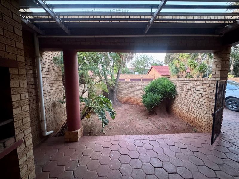 Covered patio area featuring a built-in braai, brick walls, and paved flooring, overlooking a small private garden space.