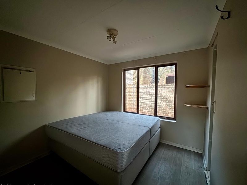 A simple bedroom featuring laminate flooring, built-in wall shelving, and a window overlooking a brick exterior wall.