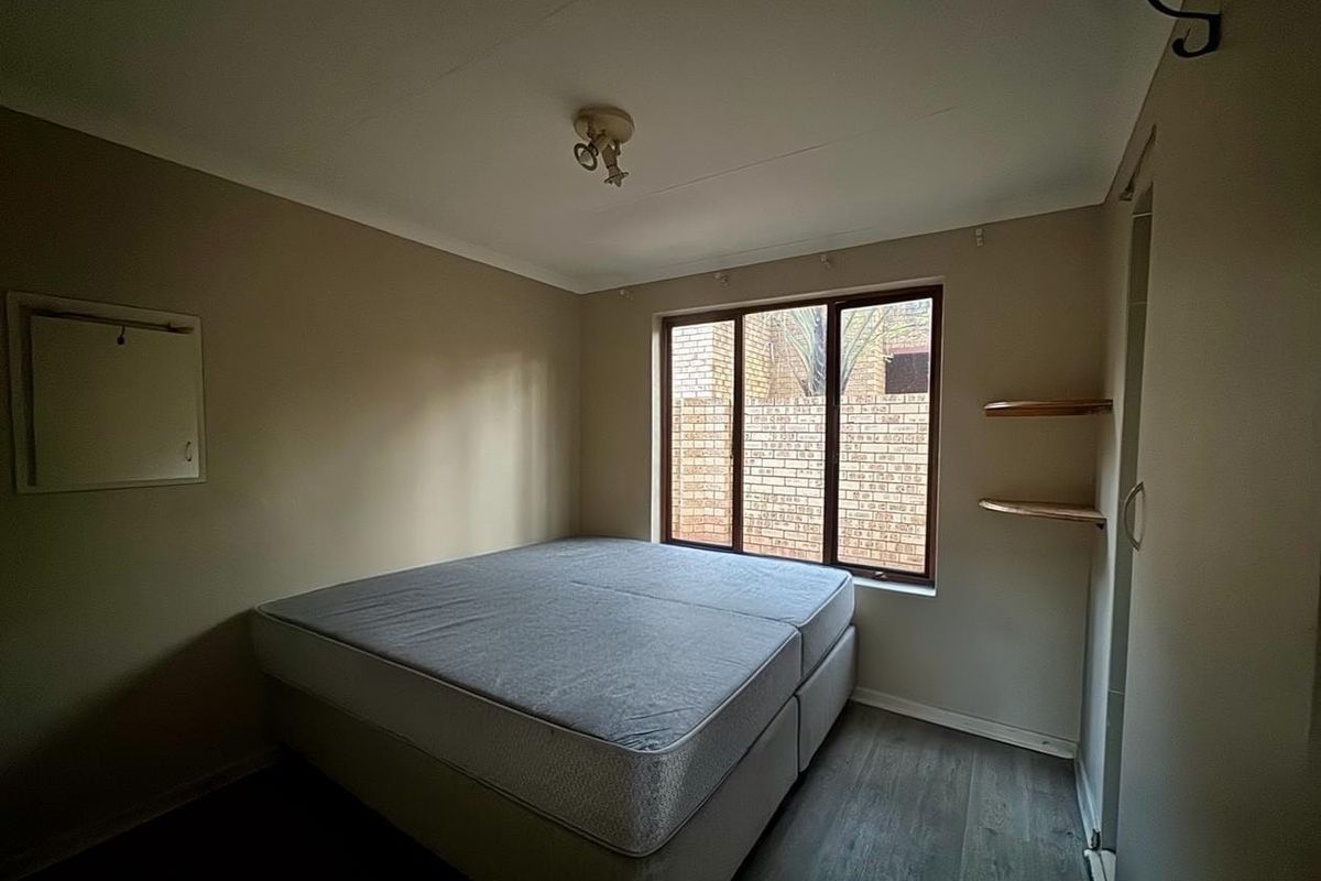 A simple bedroom featuring laminate flooring, built-in wall shelving, and a window overlooking a brick exterior wall.