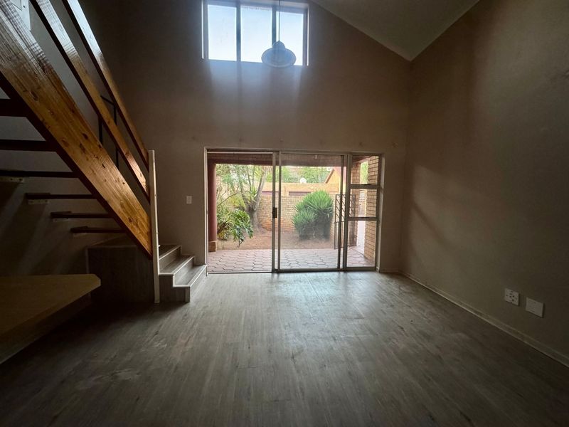 Spacious living area featuring vaulted ceilings, a wooden staircase, and large sliding glass doors providing direct access to the rear patio and garden.