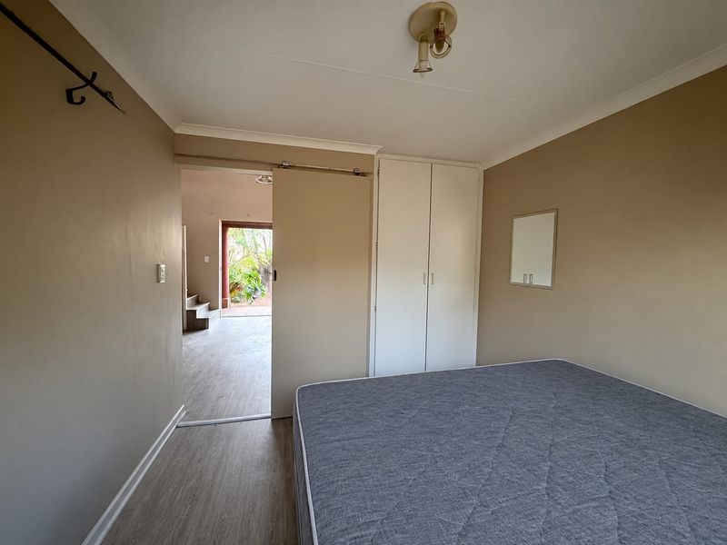 A bedroom featuring laminate flooring, a built-in wardrobe, and a sliding door leading to an adjacent living space.