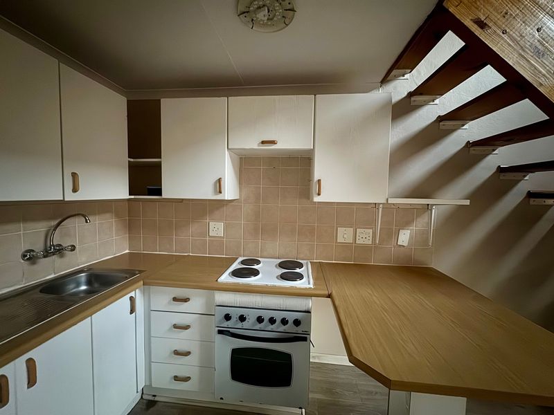 Compact kitchen featuring laminate countertops, built-in oven, electric hob, and tiled backsplash, located beneath an open staircase.