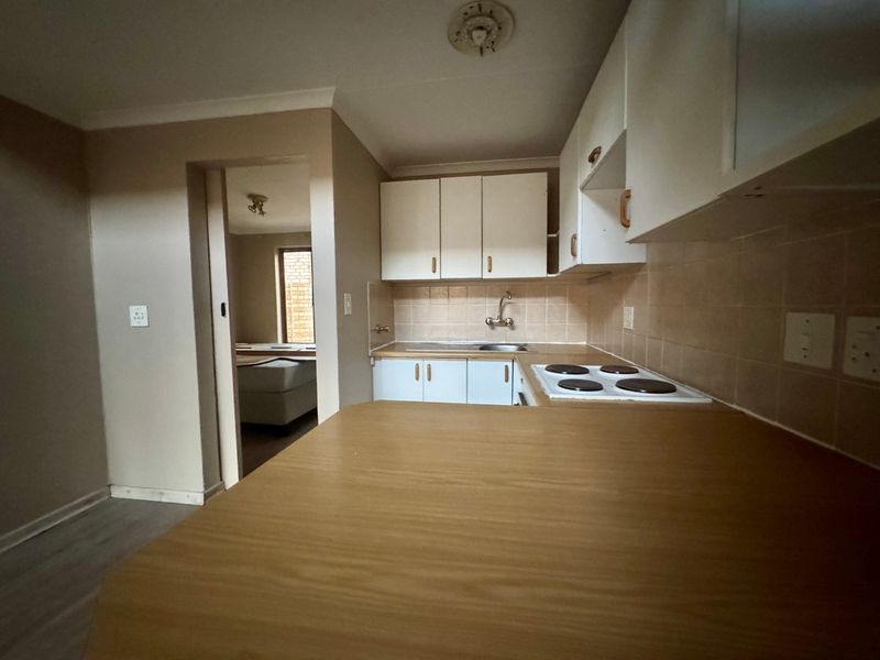 A functional kitchen featuring built-in cabinetry, laminate countertops, and an electric hob, with a view through to an adjacent room.