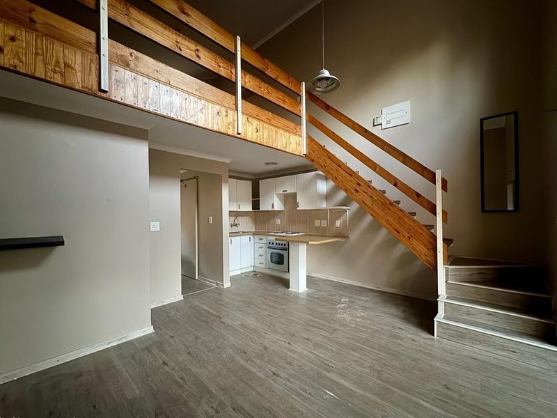 Open-plan living area featuring a mezzanine level, wooden staircase, and a compact kitchen with built-in cabinetry and appliances.