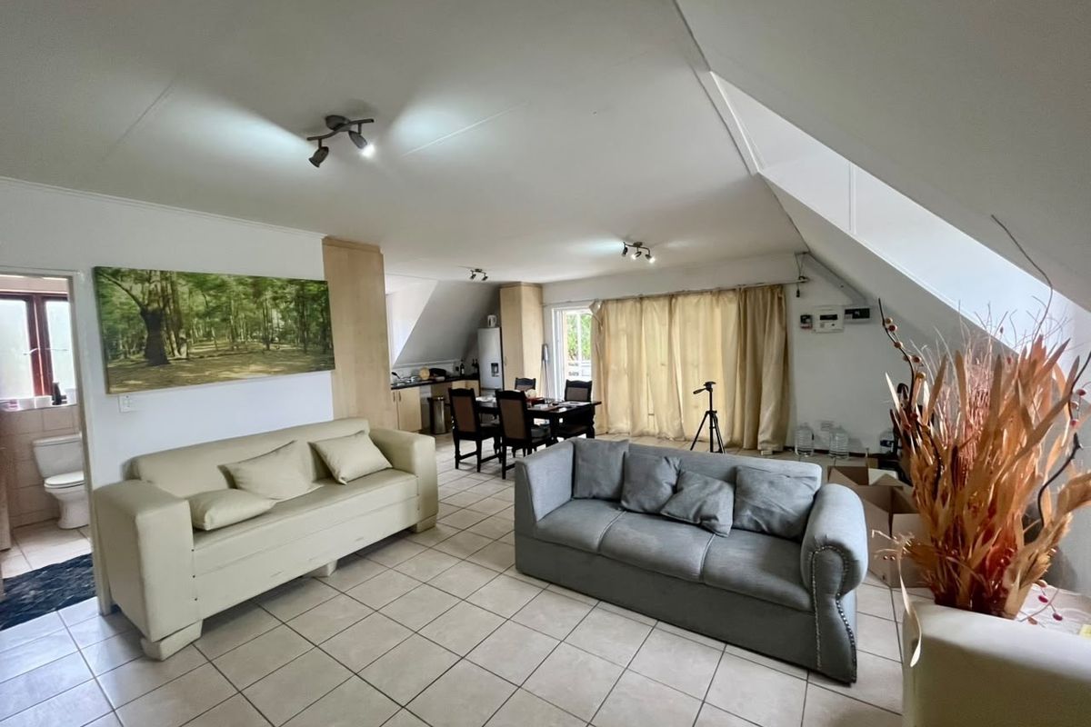 Spacious open-plan living and dining area featuring tiled floors, sloped ceilings, and an integrated kitchen space with neutral finishes.