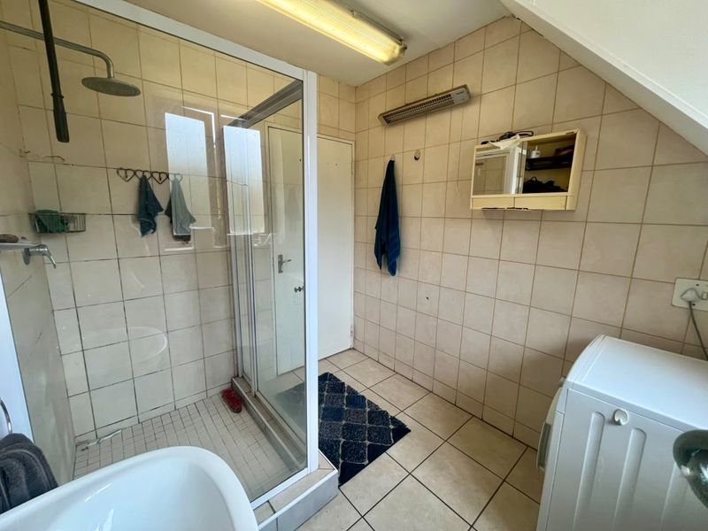A functional bathroom featuring a glass shower enclosure, tiled walls and flooring, and a wall-mounted heater, offering potential for modernization.
