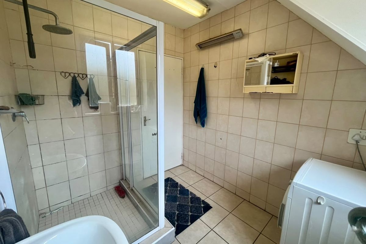 A functional bathroom featuring a glass shower enclosure, tiled walls and flooring, and a wall-mounted heater, offering potential for modernization.