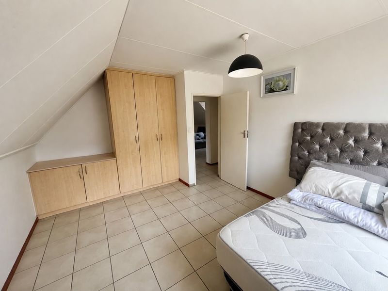 A bedroom featuring built-in wooden cupboards, tiled flooring, and a sloped ceiling, providing a functional and well-lit living space.