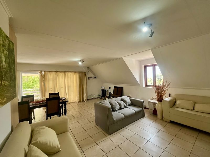 Spacious open-plan living and dining area featuring tiled flooring, sloped ceilings, and natural light from a sliding glass door and window.