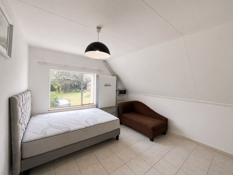 A bright bedroom featuring tiled flooring, a sloped ceiling, and a wall-mounted solar inverter system with a view of the garden.