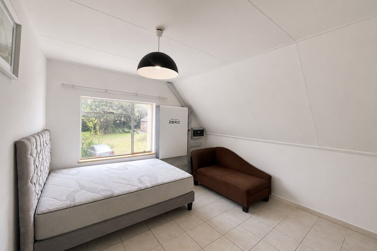 A bright bedroom featuring tiled flooring, a sloped ceiling, and a wall-mounted solar inverter system with a view of the garden.