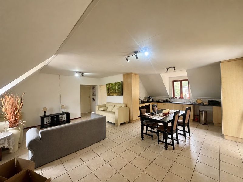 Spacious open-plan living and kitchen area featuring tiled flooring, sloped ceilings, and functional built-in cabinetry in a cottage-style layout.
