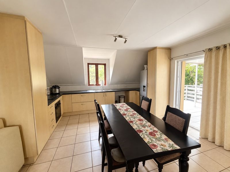 Open-plan kitchen and dining area featuring light wood cabinetry, tiled flooring, and direct access to an outdoor patio through sliding glass doors.