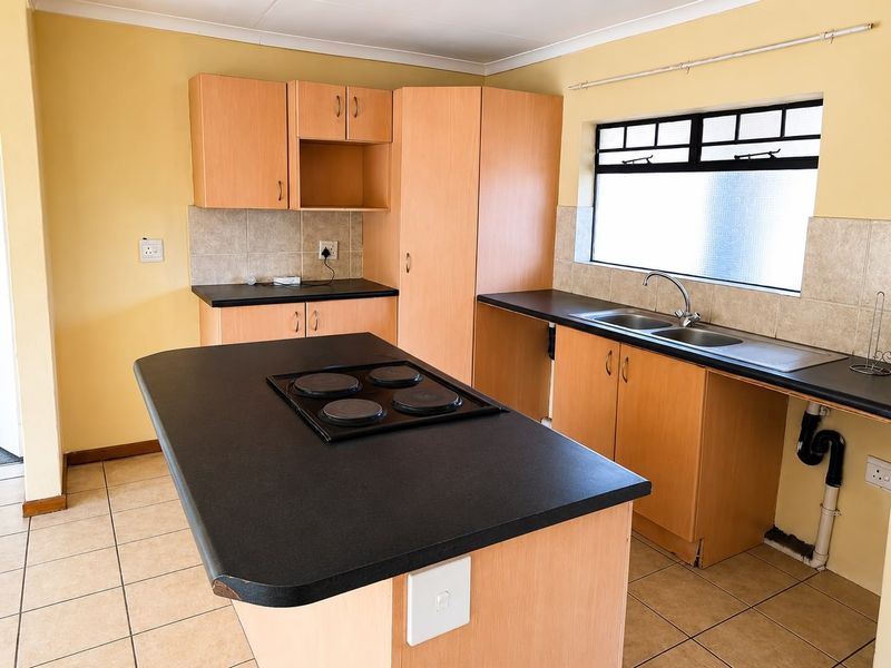 A functional kitchen featuring laminate cabinetry, a central island with a built-in electric hob, double sink, and tiled flooring.