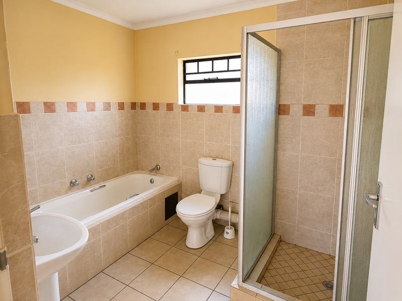 A functional bathroom featuring a built-in bathtub, separate shower enclosure, pedestal sink, and toilet with neutral wall and floor tiling.