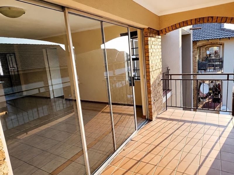A spacious covered balcony featuring tiled flooring, a decorative brick archway, and large sliding glass doors leading into the apartment interior.