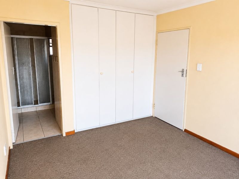 A clean, empty bedroom featuring neutral walls, carpeted flooring, and ample built-in cupboard storage, with direct access to an en-suite bathroom.