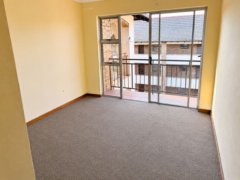 An empty bedroom featuring neutral walls, carpet flooring, and a sliding glass door providing access to a private balcony.