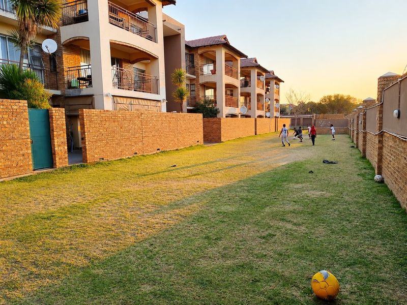 A view of the rear exterior of an apartment complex featuring a shared lawn area and brick boundary walls.