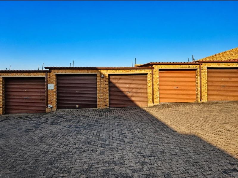 A row of secure brick-built garages featuring individual roller shutter doors and a paved driveway area.