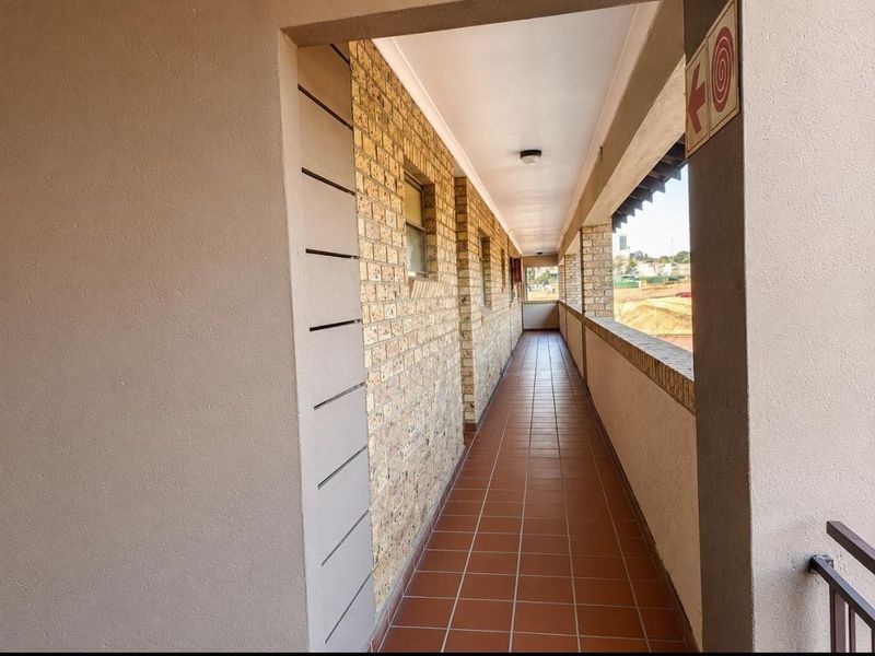 An exterior apartment hallway featuring face brick walls, tiled flooring, and a brick balustrade overlooking the surrounding area.