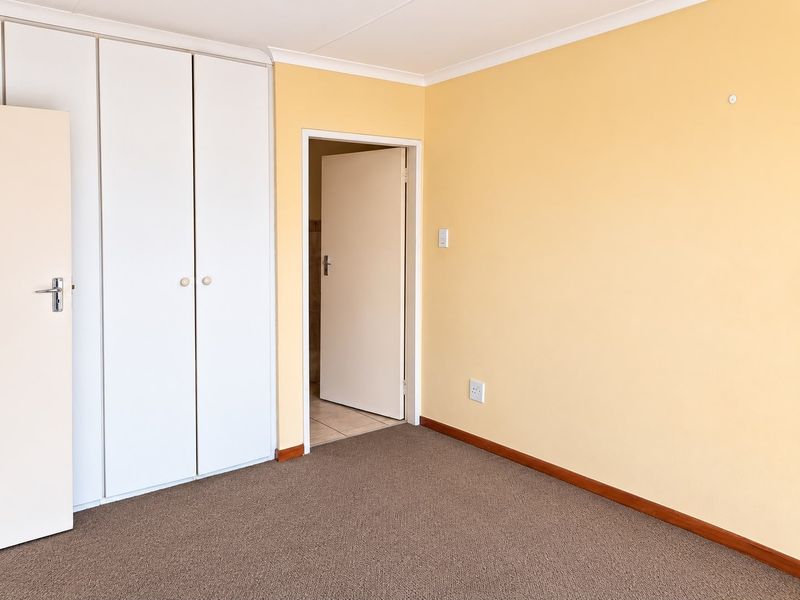 A clean, empty bedroom featuring neutral yellow walls, fitted built-in cupboards, and carpeted flooring, offering a blank canvas for personalization.