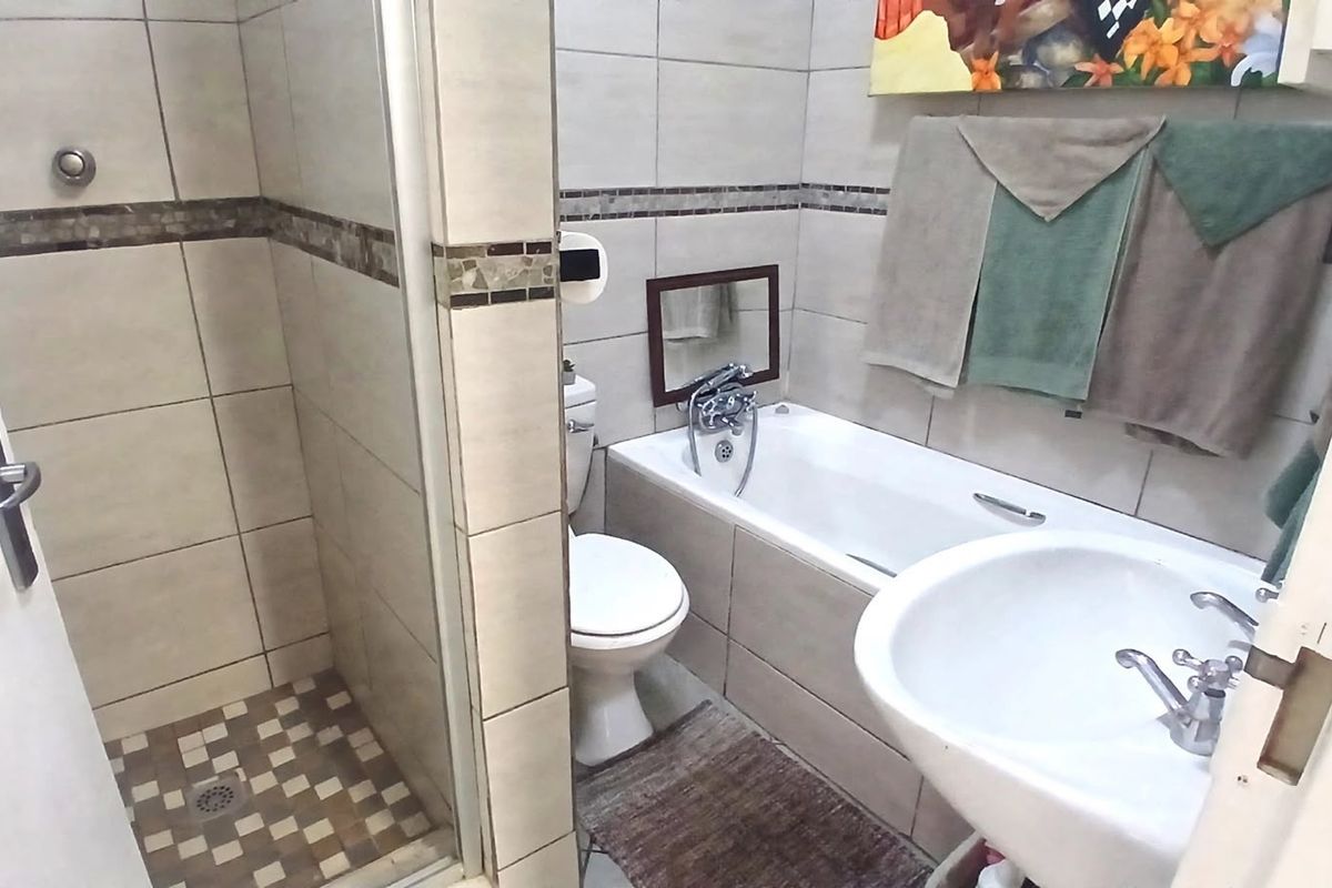 A functional bathroom featuring a shower enclosure, bathtub, pedestal basin, and toilet with neutral wall and floor tiling.