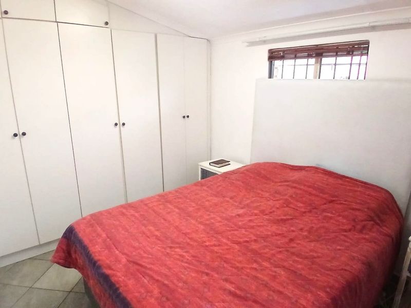 A functional bedroom featuring extensive built-in cupboard storage, tiled flooring, and a window with security bars.