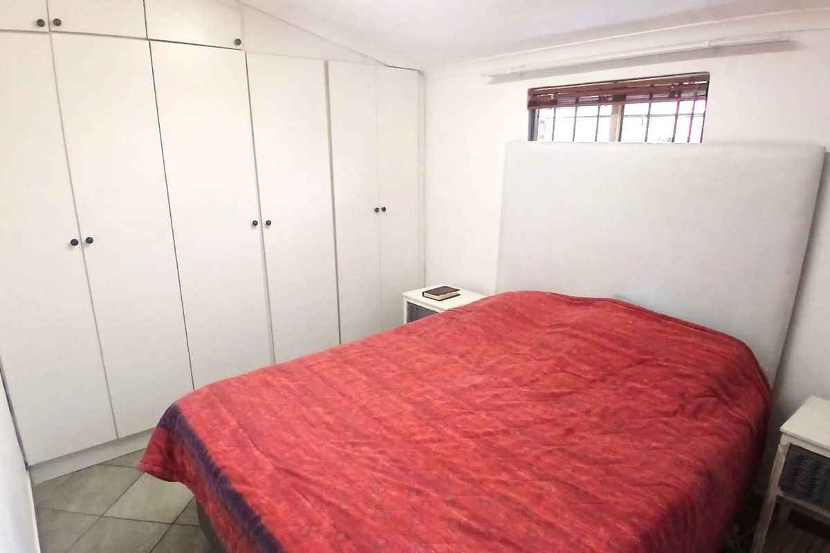 A functional bedroom featuring extensive built-in cupboard storage, tiled flooring, and a window with security bars.