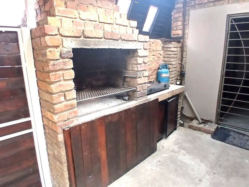 Outdoor patio area featuring a built-in brick braai, concrete countertop, and wooden storage cabinetry, providing a functional space for outdoor cooking and entertainment.