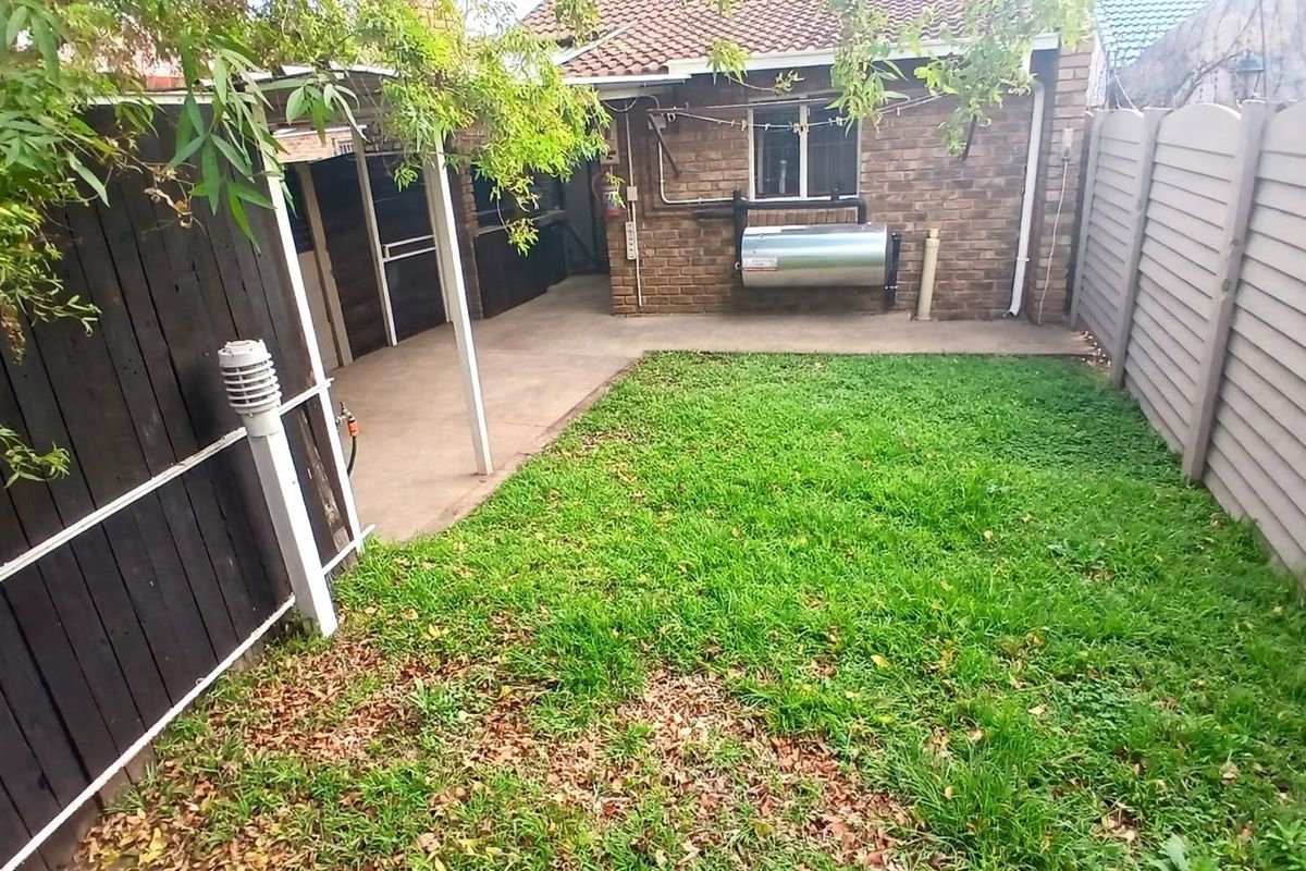 A private rear garden featuring a concrete patio area, a small lawn, and perimeter fencing, providing a functional outdoor space for the townhouse.
