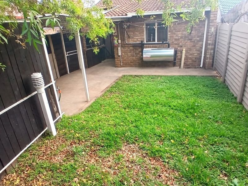 A private rear garden featuring a concrete patio area, a small lawn, and perimeter fencing, providing a functional outdoor space for the townhouse.